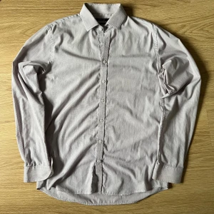 Randig skjorta från Dressmann - Säljer en stilren randig skjorta från Dressmann i en ljus färgton. Skjortan har långa ärmar och knappar framtill. Perfekt för en klassisk look.