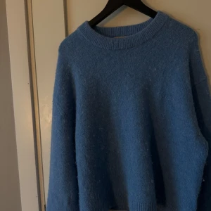 Blå stickad tröja från Gina Tricot - Mysig blå stickad tröja från Gina Tricot i storlek XS. Perfekt för kyliga dagar med sin mjuka och varma känsla. Tröjan har en klassisk rund hals och långa ärmar.