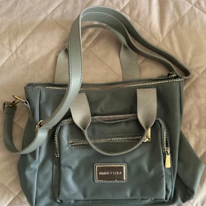 axelväska från Bimba Y Lola - Snygg axelväska från Bimba Y Lola med flera dragkedjor och justerbar axelrem. Perfekt för att bära dina dagliga nödvändigheter med stil. Väskan har en praktisk ytterficka och ett rymligt inre fack. Köpt i Spanien