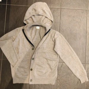 Stickad Cp Company cardigan  - Säljer en stickad cardigan/hoodie från märket Cp Company. Fint skick med  med både dubbel dragkedja och knappar. Unika detaljer vilket ger den en mysig och stilren design.