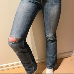 Lowwaisted jeans med hål i - Snygga blå jeans med slitningar på knäet och bakfickor med coola detaljer. De har en lågmidjad passform och en klassisk bootcut-stil. Jag skulle passa någon som är 150-155 cm och skulle säga de är i xxs. Skriv för mer frågor!
