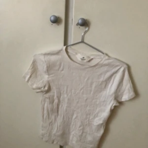 Vit ribbad topp från H&M - Säljer en vit ribbad topp från H&M. Den har korta ärmar och en rund halsringning. Perfekt för en avslappnad stil.