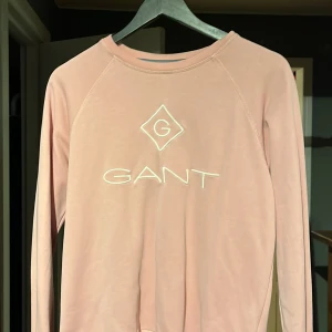 Rosa långärmad tröja från GANT - Säljer en snygg rosa långärmad tröja från GANT med deras logga broderad på framsidan. Perfekt för en avslappnad stil. Tröjan är tillverkad i ett mjukt material och har en klassisk rund halsringning.