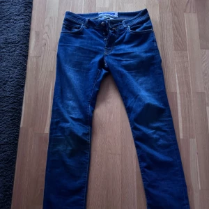 Blå jeans från Jacob Cohen - Snygga blå jeans från Jacob Cohen med klassisk femficksdesign och en röd etikett bak. De har en dragkedja och knapp framtill. Perfekta för en stilren look. Storleken är 32 och skicket är 10/10 knappast använda 