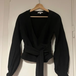 Svart omlottopp från & Other Stories - Elegant svart omlottopp från & Other Stories med långa ärmar och knytning i midjan. Inköpt för ca 1000 kr. 