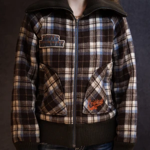 Rutig vintage jacka  - Vintage rutig jacka i brunt, blått och vitt med dragkedja framtill. Jackan har långa ärmar och ribbade muddar vid ärmslut och nederkant. Två fickor framtill med broderade detaljer. Jättesnygg!