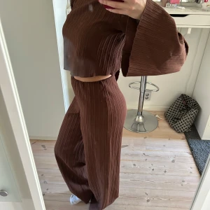 Brunt set - Snygg brun ribbad byxdress med vida ben och croppad topp. Perfekt för en stilren look med bekväm passform. Byxdressen har långa ärmar och en hög midja som ger en modern siluett.