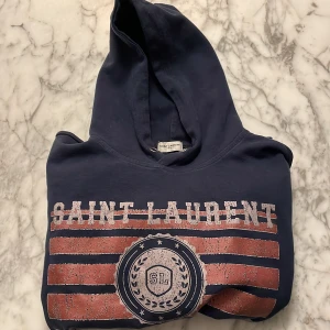 Mörkblå hoodie från Saint Laurent - Hej! Jag säljer denna riktigt feta och sällsynta hoodie från saint Laurent! Tröjan är i storlek M men passar S/ dig som är 167-170 cm! En defekt är att tagen är borta pga tvätten. Nypris på denna tröja ligger på runt 7000 kr! Hör av er om ni har frågor!😊