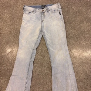 Ljusblå jeans från Silver - Säljer ett par ljusblå jeans från Silver med snygga detaljer på bakfickorna och en unik knapp. Jeansen har en klassisk femficksdesign och är perfekta för en avslappnad stil.