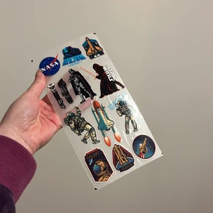 Klistermärken med rymdtema - Ett ark med klistermärken med rymdtema, inklusive NASA-logga, Star Wars-karaktärer, astronauter och rymdfärjor. Perfekt för att dekorera anteckningsböcker, laptops eller andra ytor för den rymdintresserade.