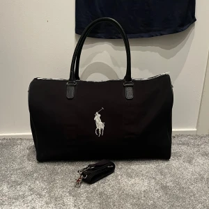Polo raulph lauren Duffel Bag!! - Ett riktigt stilren väska från polo raulph lauren. Väskan är riktigt snygg och elegant. Väskan är i färgen svart silver. Band med kommer också såklart hör av er vid minsta lilla fråga MVH Ville 