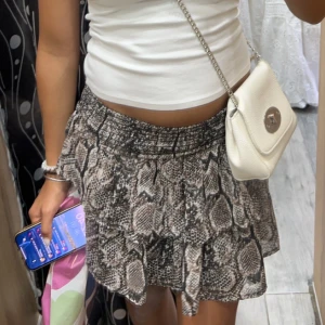 Ormmönstrad kortkjol - Trendig kortkjol med ormmönster i beige och bruna toner. Kjolen har en volangdetalj som ger en extra touch. Perfekt för att skapa en stilfull look.