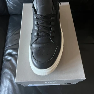 Svarta sneakers från Gram - Snygga svarta sneakers från Gram i skinn med vit sula. Skorna har klassisk snörning och en stilren design som passar perfekt till vardags. Modellen är 374g och kommer i originalkartong.