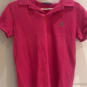 Rosa pikétröja från Ralph Lauren - Säljer en klassisk rosa pikétröja från Ralph Lauren i 100% bomull. Tröjan har en liten grön logotyp på bröstet och korta ärmar. Perfekt för en avslappnad stil. Har typ inte använt den, Bara låg i min garderob!