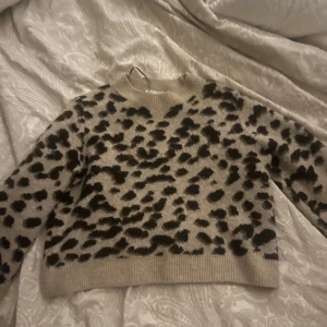 Beige leopardmönstrad tröja från H&M - Säljer en snygg beige tröja från H&M med leopardmönster i svart. Tröjan har långa ärmar och en rund halsringning. Perfekt för att ge din outfit en trendig touch. 🐆