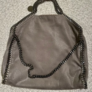 Stella McCartney Falabella tote stor - Fint skick. Hittar bara lite slitage på kedja handtag. Se närbild handtag. Modell Falabella tote foldover. Material Yttre: polyuretan 70%, polyester 30% Foder:. polyester 100% Höjd	36 cm Bredd	37 cm Djup	9 cm Handtag	11 cm Rem	22 cm