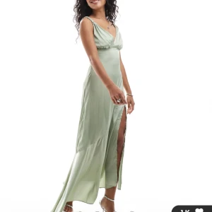 Ljusgrön långklänning med slits - Elegant ljusgrön långklänning i satin med smala axelband och djup v-ringning. Klänningen har en  slits på sidan som gör den lätt att dansa i. Oanvänd med lapparna kvar då jag missade att returnera den i tid. Nypris 969kr