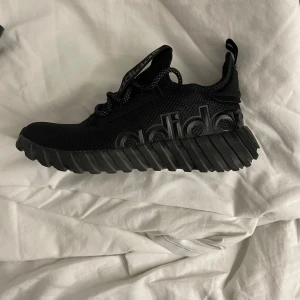 Svarta sneakers från Adidas - Snygga svarta sneakers från Adidas med en unik sula och tydlig logga på sidan. Skorna har snörning och är tillverkade i ett syntetmaterial som ger en modern look.