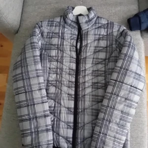 Grå rutig pufferjacka - Snygg grå pufferjacka från Charles Vögele med ett stilrent rutigt mönster. Jackan har en dragkedja framtill och är perfekt för kyligare dagar. Den quiltade designen ger extra värme och komfort.