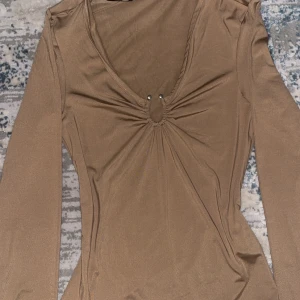 Beige långärmad topp från H&M - Säljer en stilren beige långärmad topp från H&M. Toppen har en v-ringad design med rynkdetaljer vid halsen. Perfekt för en chic och bekväm look. Passar bra för eleganta eller festliga looks men även en lite finare vardagslook. Aldrig använd.