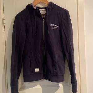 Mörkblå huvtröja från Race Marine - Snygg marinblå kofta från Race Marine med dragkedja och tryck på bröstet. Tröjan har långa ärmar och en randig insida i huvan.  Bra skick 