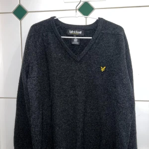 Mörkgrå tröja från Lyle & Scott - Säljer en stilren mörkgrå tröja från Lyle & Scott med v-ringning och deras ikoniska logga på bröstet. Perfekt för kyligare dagar och passar till många olika outfits.
