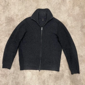 Svart stickad tröja från Massimo Dutti - Säljer en stilren svart/mörkgrå stickad tröja från Massimo Dutti. Tröjan har en dragkedja framtill och en hög krage som ger extra värme. Perfekt för kyliga dagar. Nypris ~1200kr, mitt pris: 599kr. Perfekt skick men lite nopprig, vilket enkelt går att fixa. Storlek M. 