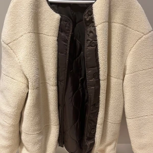 Beige teddyjacka från Samsøe Samsøe - Mysig beige teddyjacka från Samsøe Samsøe med quiltad insida och knappar framtill. Perfekt för kyliga dagar när du vill hålla dig varm och stilren.