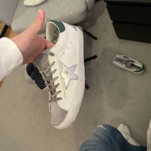 Golden goose nya - Snygga Golden Goose sneakers i vitt med grå detaljer på mockan, skorna är nästintill nya och säljer för ett bra peng, NYPRIS 7000kr så passa på! ALLT OG FÖLJS MED box dustbag och även golden goose äkthetsbrevet 