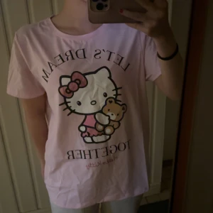 Rosa Hello Kitty t-shirt - Söt rosa t-shirt med Hello Kitty-tryck och texten 'Let's Dream Together'. Perfekt för alla Hello Kitty-fans som vill ha en bekväm och stilren look. Tröjan är i storlek S men passar även dig som har storlek M