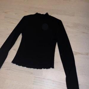Svart långärmad topp - Snygg svart långärmad topp med hög krage och vågig kantdetalj. 
