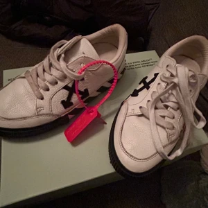 Vita sneakers med svarta detaljer från Off-White - Off-White Arrow Low Vulcanized – White/Black (Storlek 35, passar 36)  Säljer mina Off-White Arrow Low Vulcanized sneakers i färgen White/Black. 	•	Storlek: 35 (passar även 36) 	•	Skick: Använda 4 gånger, i mycket bra skick. 	•	Originaldetaljer: Låda och skosnören med texten “SHOELACES” finns kvar. 	•	Passform: Bekväma och stilrena sneakers som passar både vardag och fest.  Nypris ligger på ca 4000 kr. Jag säljer dem för 2500 kr,