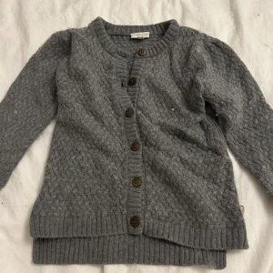 Grå stickad kofta från Pomp de Lux - Mysig grå stickad kofta från Pomp de Lux med knappar framtill. Koftan har ett fint texturerat mönster och ribbstickade kanter. Perfekt för kyliga dagar. Den kommer tvättas och strykas innan den skickas! ⭐️