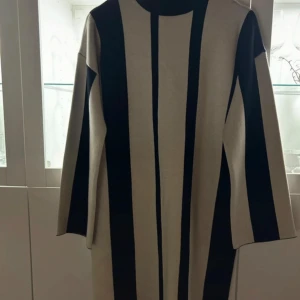 Randig klänning från Vero Moda - Snygg klänning från Vero Moda med breda svarta och beige ränder. Den har en avslappnad passform och långa ärmar, perfekt för en stilren look. Oanvänd då storleken ej passade.