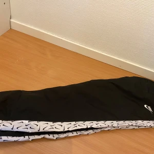 Svarta träningsbyxor och Hoodie från Nike - Snygga svarta träningsbyxor från Nike med vita detaljer och logotyp. Byxorna har elastisk midja och är perfekta för sport och träning. De har ett unikt mönster längs sidorna som ger en cool look. Och de fantastiska sköna vinter hoodie från Nike. Helt ny trakcksuit