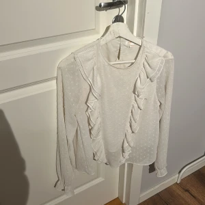 Vit blus från gina tricot - Säljer en fin oanvänd blus från gina tricot med volanger perfekt till en vardags och fest look!