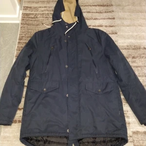 Mörkblå jacka från Indigo - Säljer en mörkblå jacka från Indigo med quiltad insida och dragkedja. Jackan har långa ärmar och flera praktiska fickor. Perfekt för kyliga dagar.