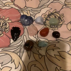 Samling av olika stenar och kristaller - En vacker samling av olika kristaller i olika färger och former. Inkluderar en hjärtformad blå kristall, en svart pilspetsformad kristall, samt flera andra i nyanser av rött, grönt och blått. Perfekt för samlare eller som dekoration. Osäker om dom är äkta.