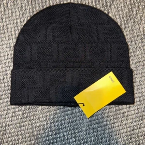 Svart stickad mössa från Fendi - Snygg svart stickad mössa från Fendi med ett diskret mönster. Perfekt för att hålla värmen under kyliga dagar. Mössan har en uppvikt kant för extra stil och komfort. 