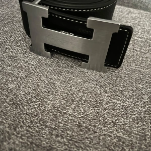 BÄLTE - Snyggt svart skärp med ett stilrent H-format spänne i silver. Skärpet är tillverkat i skinn och har vita sömmar som ger en fin kontrast. Få repor priset kan diskuteras genom snabb affär.