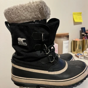 Svarta vinterstövlar från Sorel - Säljer ett par svarta vinterstövlar från Sorel med beige detaljer och snörning. Stövlarna är vattentäta och har en varm, fluffig insida för extra komfort under kalla dagar. Nypris 2200kr.