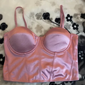 Rosa satin korsett -  Rosa korsett i satin med justerbara axelband och dragkedja. 