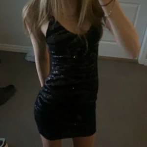 Svart glittrig klänning - Snygg svart glittrig klänning med tight passform. Perfekt för en utekväll eller fest. Klänningen är ärmlös och kort, vilket ger en elegant och stilren look.