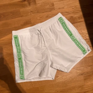 Vita shorts från Emporio Armani - Snygga vita shorts från Emporio Armani med gröna detaljer längs sidorna. De har en bekväm resårmidja och snörning för justerbar passform. Perfekta för en avslappnad stil.