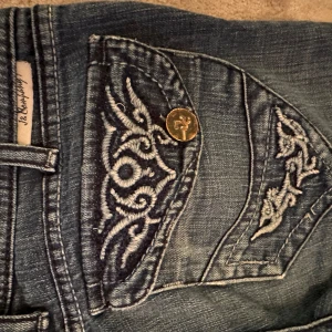 Blå jeans med broderade fickor - Säljer ett par snygga blå jeans med coola broderade detaljer på bakfickorna. Jeansen har en klassisk femficksdesign och är i en skön denimkvalitet. Perfekta för en avslappnad vardagslook!