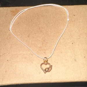 Armband med hjärthänge - Säljer ett enkelt och stilrent armband med ett guldigt hjärthänge. Hänget har en liten vinge på sidan vilket ger det en unik touch. Perfekt för vardagsbruk eller som en söt detalj till en festoutfit.