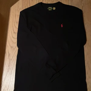Svart långärmad tröja från Ralph Lauren - Säljer en stilren svart långärmad tröja från Ralph Lauren. Den har en klassisk passform och har den klassiska röda loggan. Perfekt för både vardag och lite finare tillfällen. Tröjan är i nyskick och redo för en ny ägare. Pris kan diskuteras!