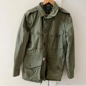 Grön jacka från Polo Ralph Lauren - Säljer en stilren grön jacka från Polo Ralph Lauren. Jackan har långa ärmar och knappar framtill. Den är perfekt för höst och vår med sin klassiska design och praktiska fickor. Har inga defekter.