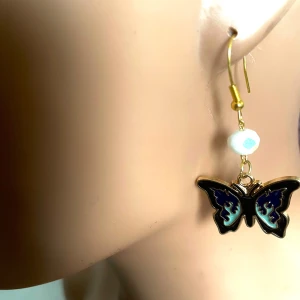 By prisförslag- 1 st Svart fjärilsörhänge med vit pärla - Elegant örhängen med en svart fjärilsdesign och en vit pärla ovanför. Örhänget har en krok i guldton för enkel användning. Perfekta för att lägga till en subtil men stilfull touch till din look.