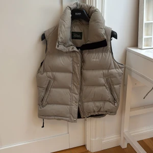 Beige dunväst från Peak Performance - Säljer en snygg beige dunväst från Peak Performance. Västen har dragkedja och praktiska fickor framtill. Västen kommer med en luva som kan tas bor med en fördrag kedja! Det är en lite äldre väst så den är lite smutsig på sina ställen men det går säkert att tvätta bort. Det är storlek M men den passar även S skulle jag säga. Skriv för fler frågor!